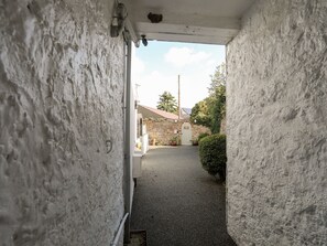 Une ruelle étroite, avec un bâtiment en pierre et un mur blanc d’un côté.