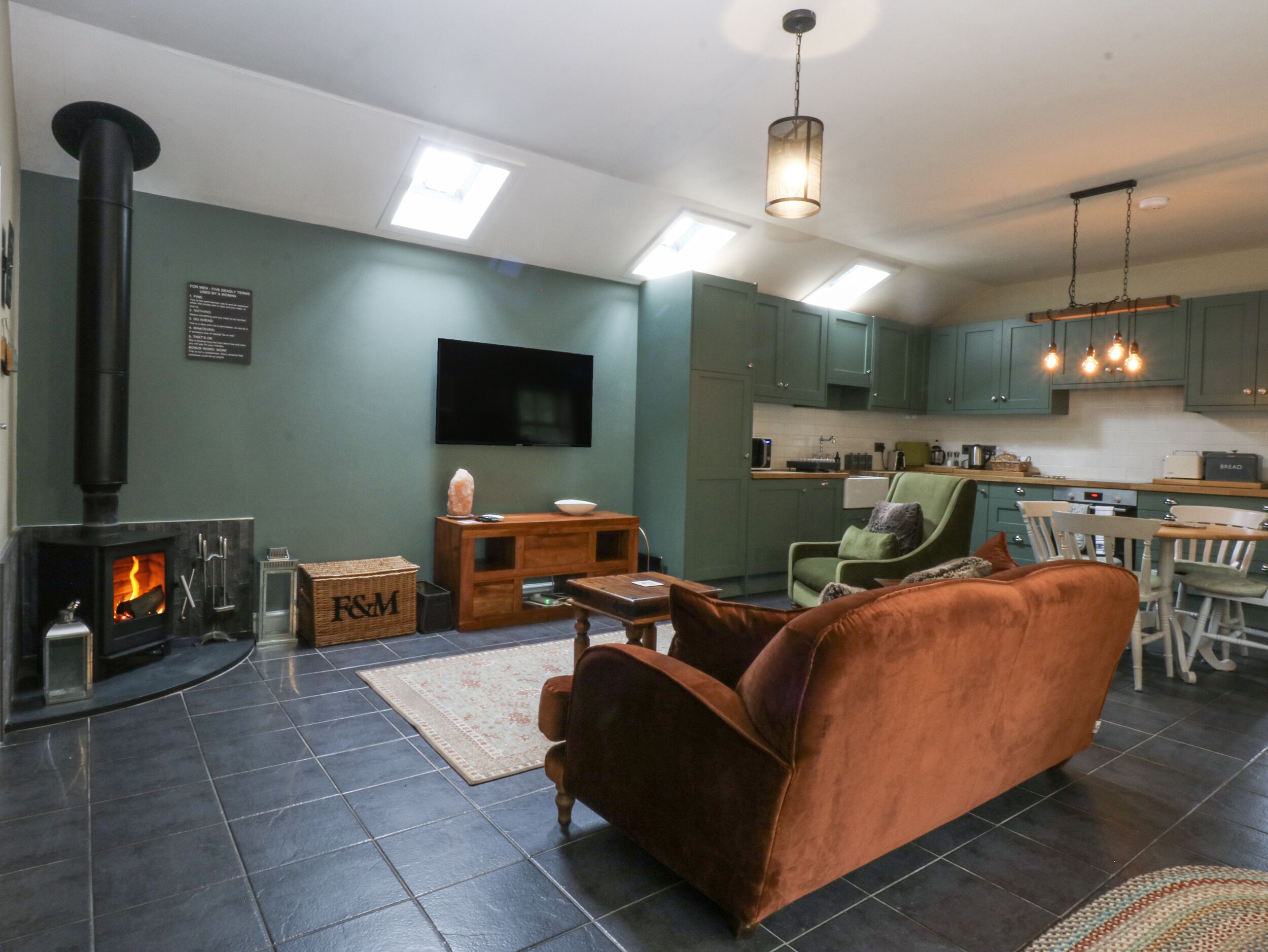 Ein Wohnzimmer mit Kamin, Fernseher und Essbereich, im Hintergrund eine Küche.