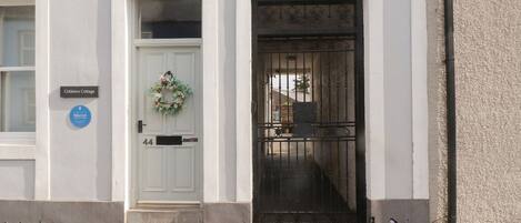 A building with a white facade, a door with a wreath, and a black gate.