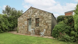Une petite maison en pierre avec une pelouse et deux chaises pliantes blanches.