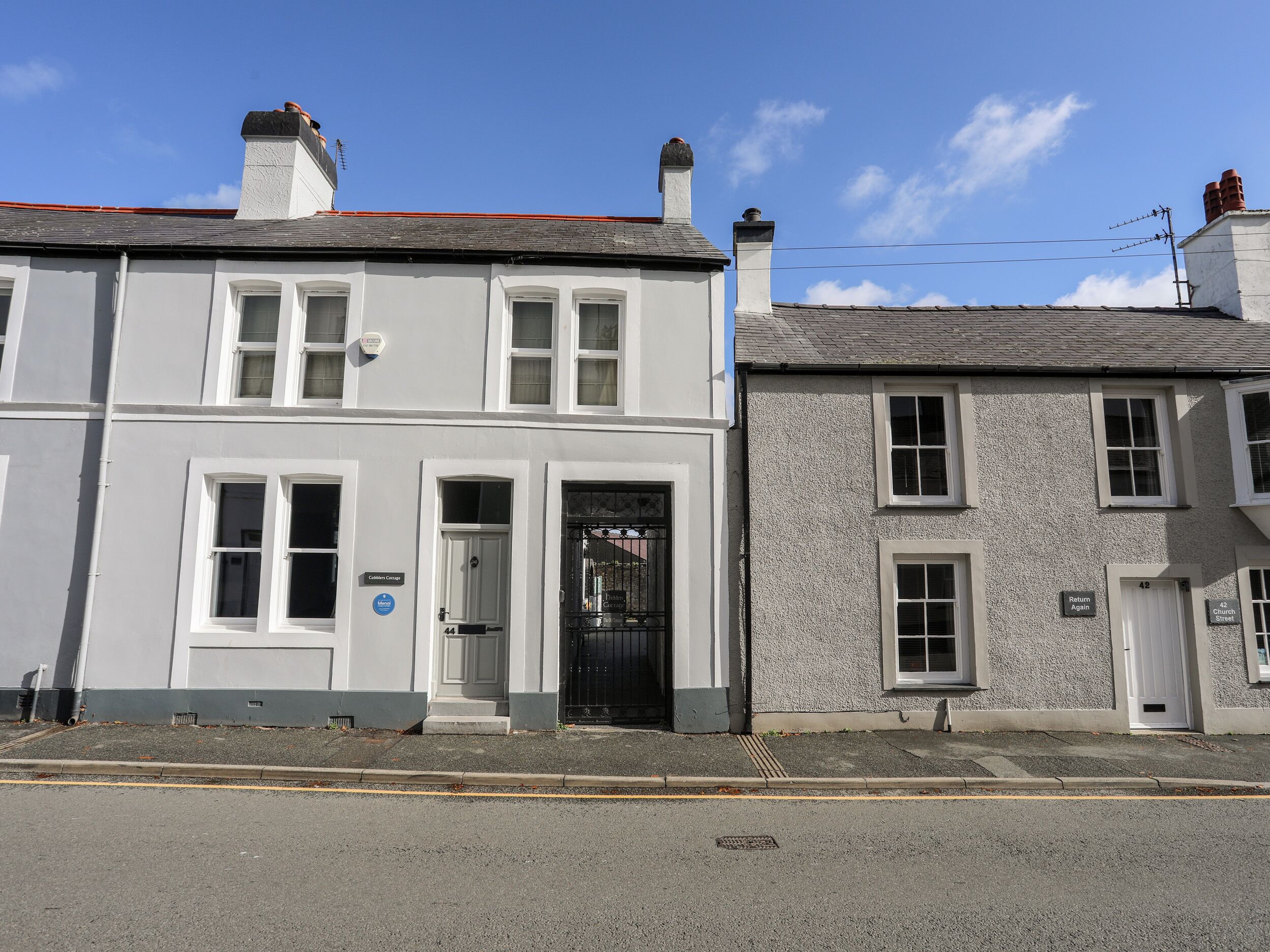 A two-story building with a white facade, a black gate, and a clear blue sky.