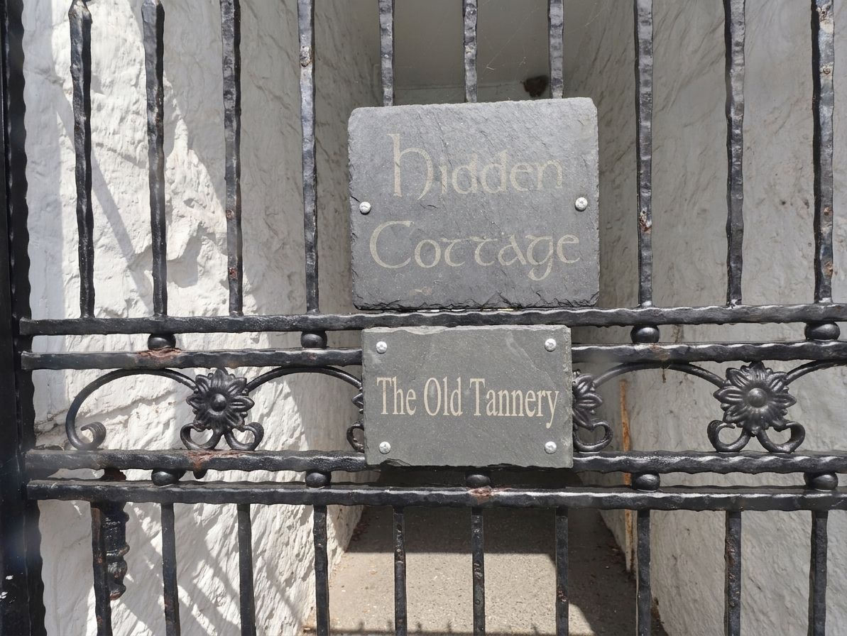 Un cancello in ferro battuto con due cartelli: 'Hidden Cottage' e 'The Old Tannery'.