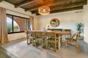 A dining area with a wooden table and chairs, a hanging light fixture, a mirror, and a view through a window. - 5 King Beds, City/Mountain Views, Pool, 1 story ranch-style home, foothills (Catalina Foothills)