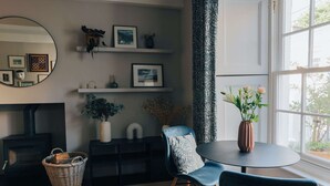 Ein gemütliches Wohnzimmer mit Kamin, einem runden Tisch mit Blumenvase und einem blauen Sessel.