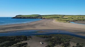 Eine Küstenlandschaft mit sandigem Strand, felsigen Abschnitten und grünen Hügeln im Hintergrund.