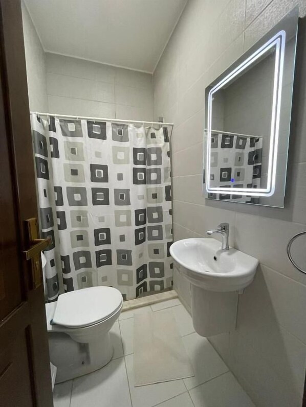 Un baño con inodoro, lavabo y cortina de ducha de estampado geométrico.