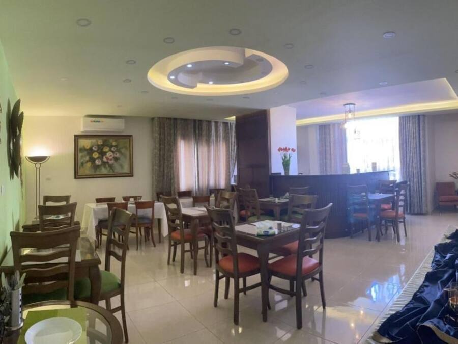 A dining area with multiple tables and chairs, a central bar area, and a large window with curtains.
