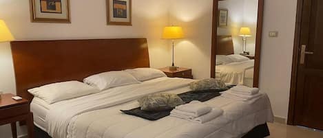 A hotel room with a large bed, two bedside tables, a mirror, and framed artwork on the wall.