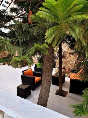 Un espacio de estar al aire libre con mobiliario de mimbre y un árbol.