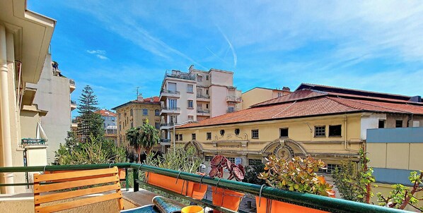 Una terraza con un banco de madera, una taza amarilla y un plato de pasteles.