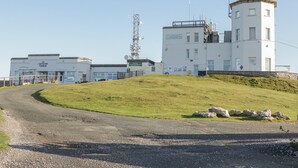A white building with a tower, a sign reading "Summit Complex," and a road curving around a grassy hill. - Apartment 2 (Llandudno)