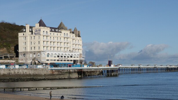 A large hotel with multiple stories and a prominent tower, located near a pier extending into the water. - Apartment 2 (Llandudno)