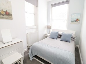 A minimalist bedroom with a bed, bedside table, and a radiator. - Apartment 2 (Llandudno)