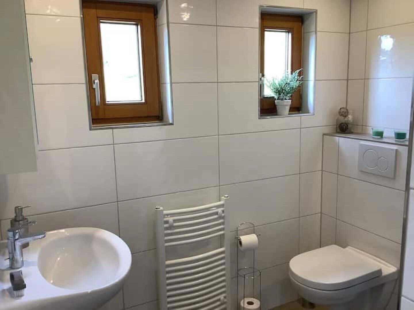 Ein modernes Badezimmer mit Waschbecken, Toilette und Handtuchhalter. Zwei Fenster sorgen für natürliches Licht.