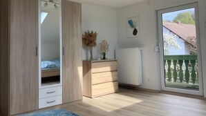 Ein Schlafzimmer mit einem Holfischschrank, einem Schminktisch, einem Heizkörper und einem Fenster mit Blick auf ein Haus und Bäume.