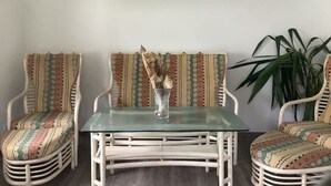 Ein Zimmer mit zwei Korbstühlen mit gemusterten Kissen, einem Glastisch und einer Topfpflanze.