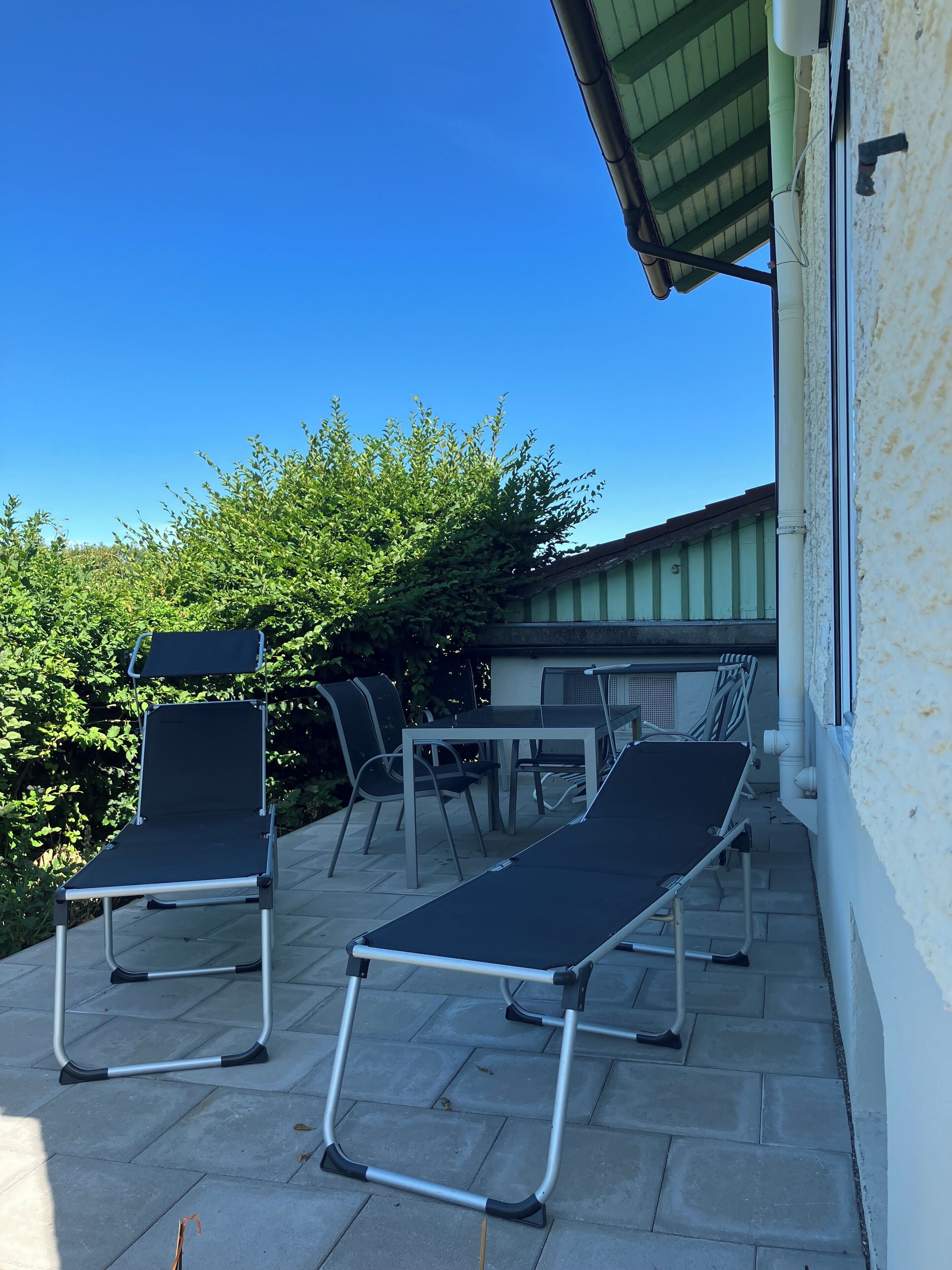 An outdoor patio with two reclining chairs, a table, and a chair with a backrest.