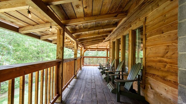 A wooden cabin with a porch, wooden benches, and a view of the surrounding forest. - Private Cabin Retreat – Relax in the Hot Tub & Cozy Up by Fire! (Pigeon Forge)