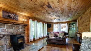 A cozy cabin interior with a stone fireplace, wooden walls, a leather sofa, and a dining area. - Private Cabin Retreat – Relax in the Hot Tub & Cozy Up by Fire! (Pigeon Forge)