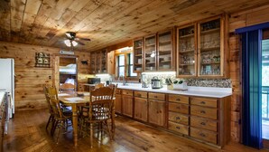A wooden cabin-style kitchen with a dining table and chairs, wooden cabinets, and a tiled backsplash. - Private Cabin Retreat – Relax in the Hot Tub & Cozy Up by Fire! (Pigeon Forge)