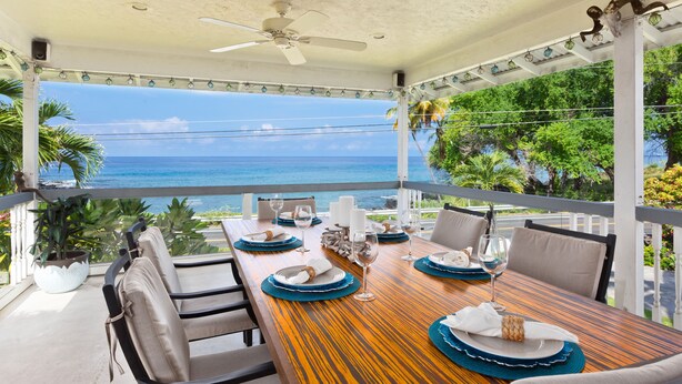 A dining area with a view of the ocean, a ceiling fan, and a table set with plates, glasses, and napkins.