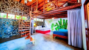 A spacious room with a stone wall, a wooden staircase, a large bed, and a blue sofa. - Jungleland at Hermosa Point. 2 Pools, A/C & Wi-Fi! Sleeps 23!
Rustic Luxury! (Playa Hermosa)