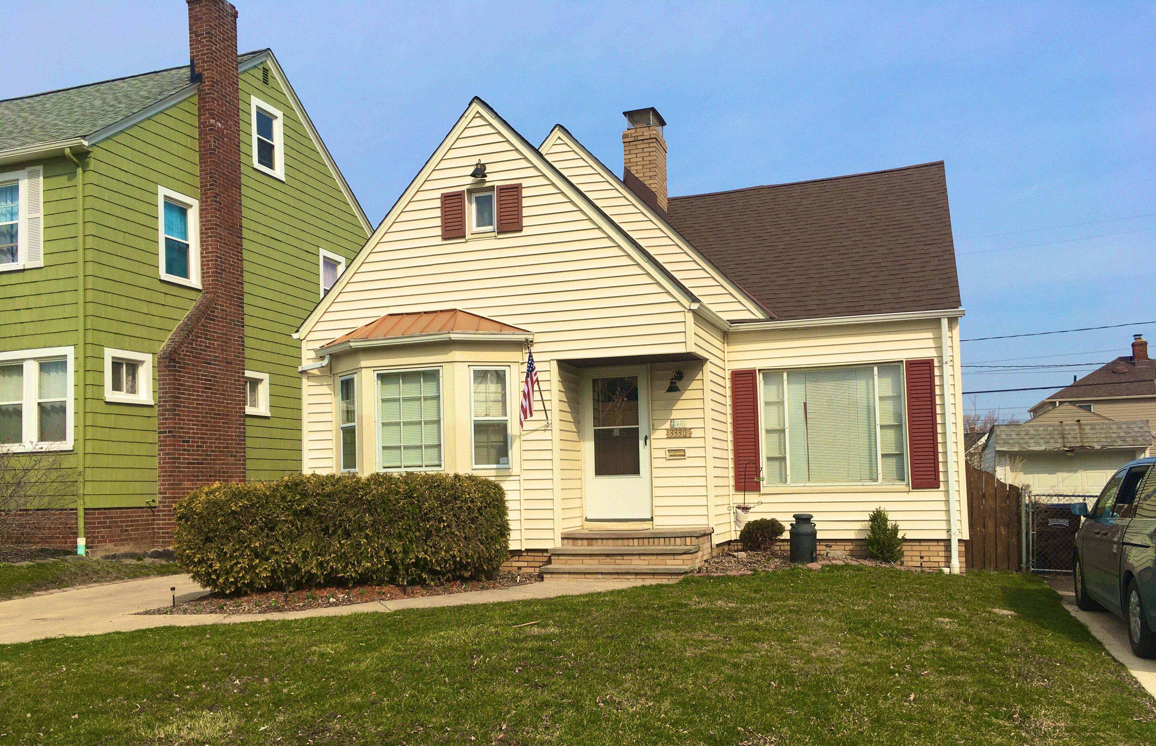 A two-story house with a front porch, a small front yard, and an American flag.