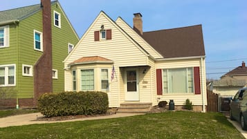 A two-story house with a front porch, a small front yard, and an American flag.