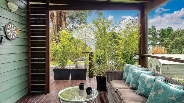 A covered outdoor area with a sofa, two black planters, and a dartboard on a green wall. - Refreshing Rainforest Retreat - Kangaroo Valley (Kangaroo Valley)