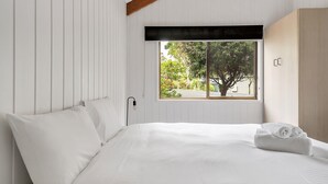 A bedroom with a bed, white linens, a window with a view of trees, and a wooden wardrobe. - Refreshing Rainforest Retreat - Kangaroo Valley (Kangaroo Valley)