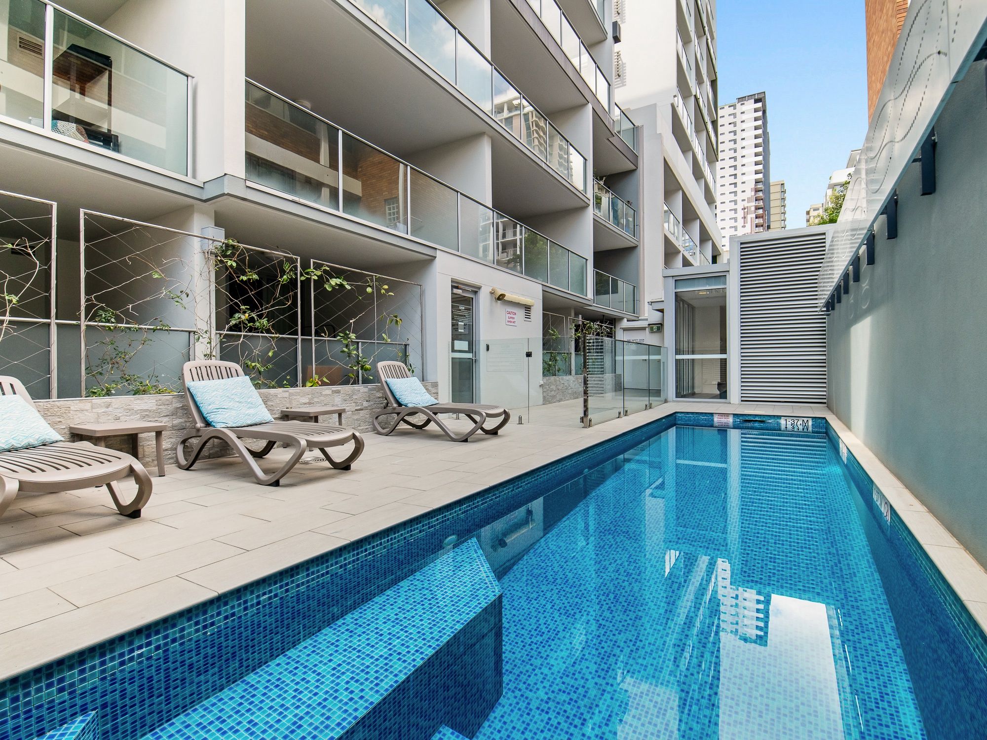 A modern outdoor swimming pool with lounge chairs and a glass balustrade.