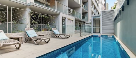 A modern outdoor swimming pool with lounge chairs and a glass balustrade.