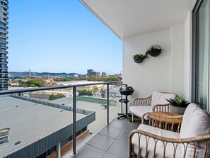 A balcony with a view of the city, wicker furniture, and a grill.