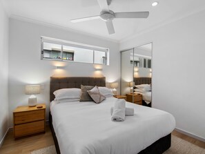 Une chambre à coucher moderne avec un lit, des tables de chevet, un ventilateur de plafond et un grand miroir.