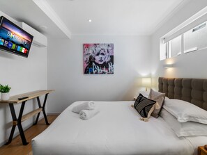 A modern hotel room with a bed, a desk, a TV, and a painting on the wall.