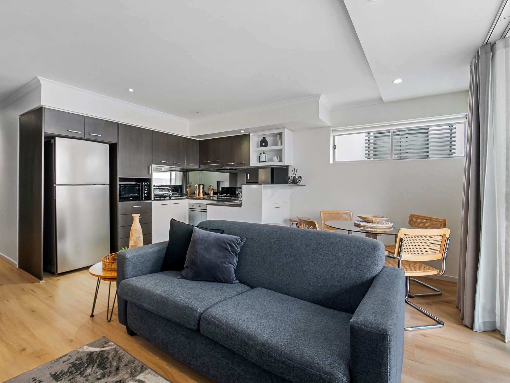 Ein modernes Apartment mit einem grauen Sofa, einem Essbereich und einer Küche.