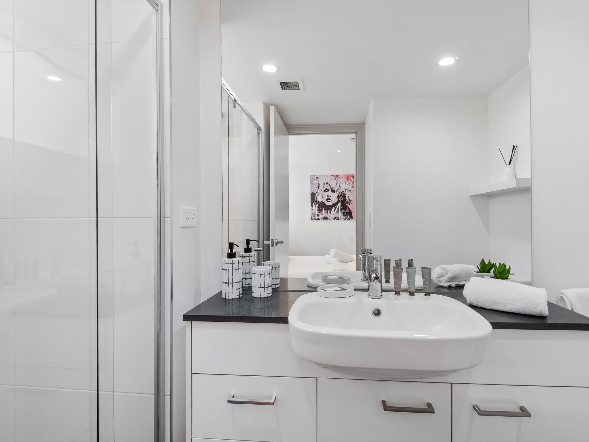 Une salle de bain moderne avec un lavabo blanc, un plan de toilette noir et un grand miroir.