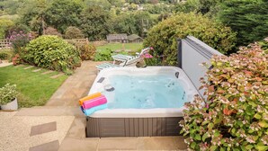 Ein Whirlpool in einem Garten mit Blick auf sanfte Hügel und Häuser im Hintergrund.
