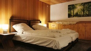 A bedroom with a wooden headboard, a bed with white linens, a nightstand with a lamp, a wooden dresser, and a painting of a forest on the wall. - Geräumige Wohnung in Altenau mit Terrasse (Altenau)