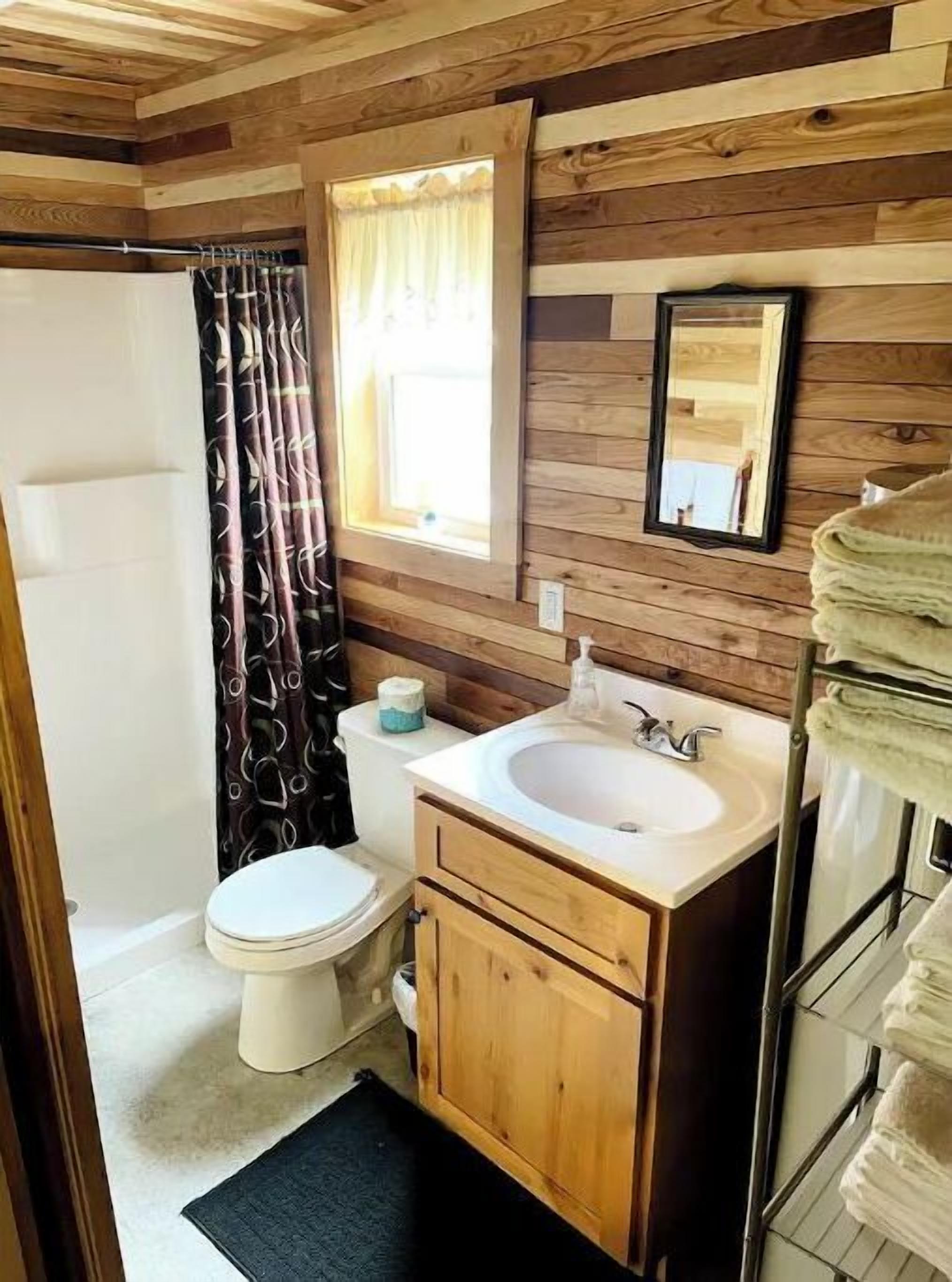 Une petite salle de bain avec un mur en bois, un lavabo blanc, des toilettes et un rideau de douche.