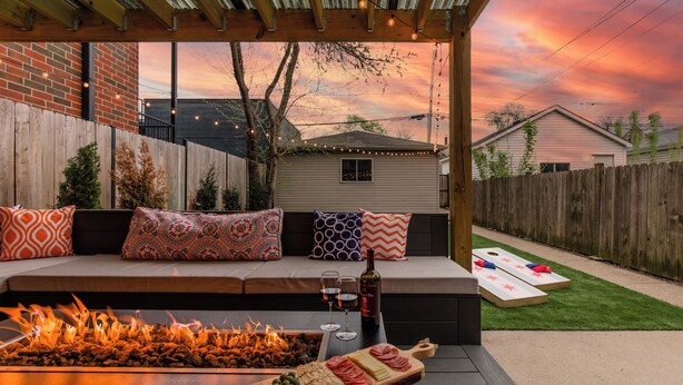 Une terrasse à l’arrière de la maison, agrémentée d’un foyer, une table en bois avec des collations et un coin salon avec des coussins à motifs.