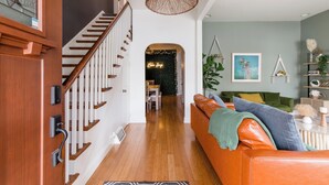 Un salon moderne avec un escalier, un mur vert et un coin repas à l’arrière-plan.