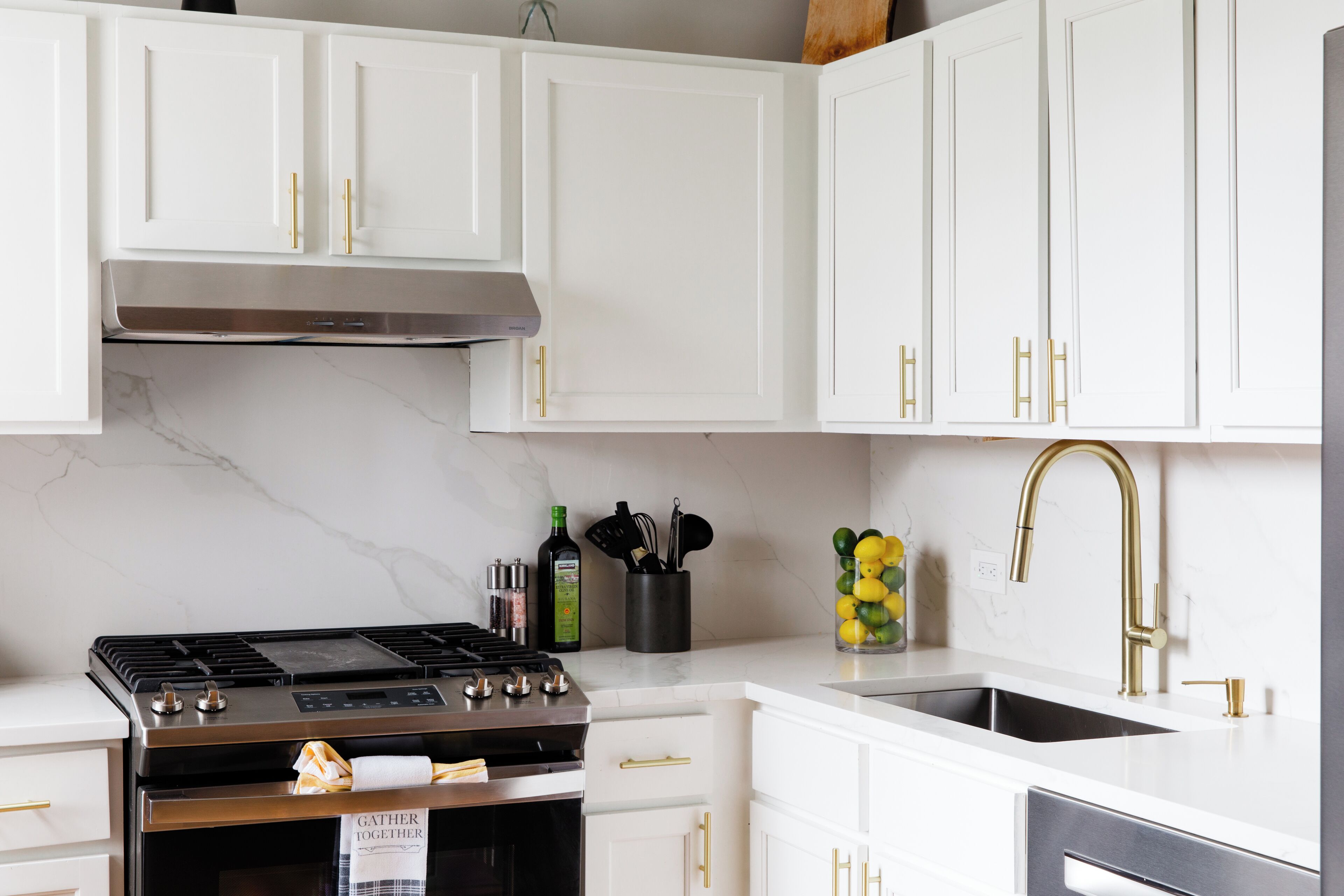 A modern kitchen with white cabinets, a stainless steel stove, and a gold faucet.