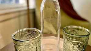 Una botella de vidrio transparente con la etiqueta "The Wilis-James Bed & Breakfast" y dos vasos de vidrio a juego sobre una mesa.