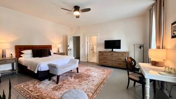 A hotel room with a bed, bedside tables, a desk, a chair, a television, and a ceiling fan.