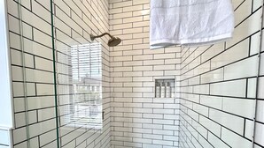 Casa de banho moderna com azulejos brancos, cabine de chuveiro em vidro e toalha pendurada na parede.