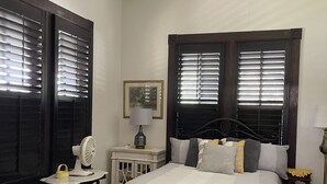 A bedroom with a bed, bedside tables, a ceiling fan, and windows with blinds.