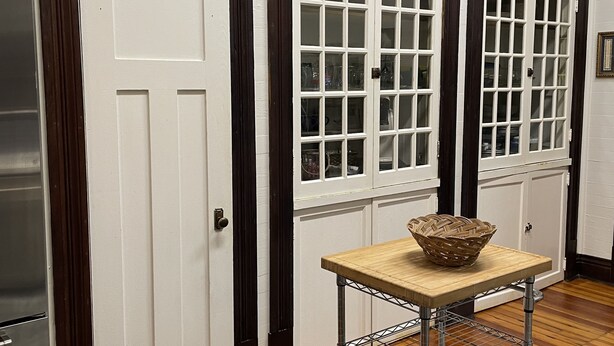 A room with a wooden floor, a metal table with a basket, and a blue rug. There are three doors with different designs.