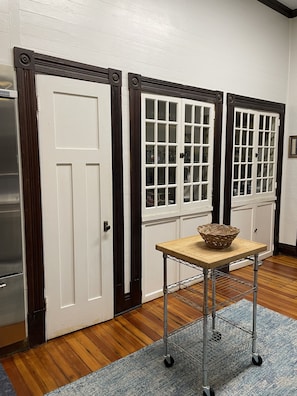 Una habitación con piso de madera, una mesa metálica con una cesta, y un tapete azul. Hay tres puertas con diseños diferentes.