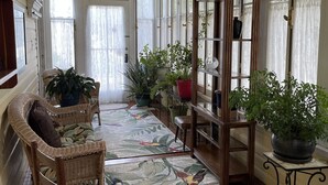 A sunlit hallway with wicker chairs, a patterned rug, and potted plants.